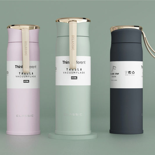 Three vacuum flasks in different colors on a gray background