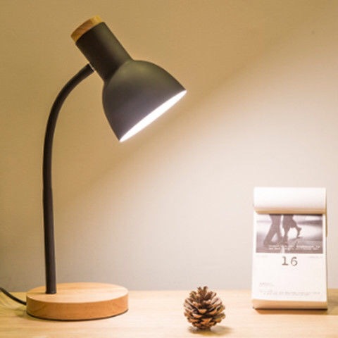 Desk lamp with wooden base on a table next to a calendar and pine cone.