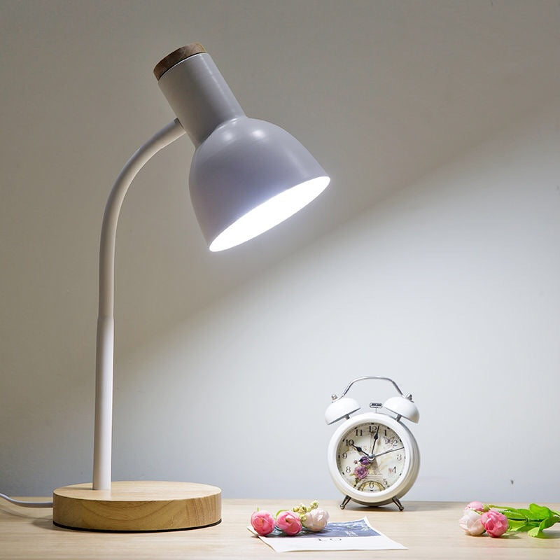 Table lamp with wooden base on a desk next to a clock and flowers