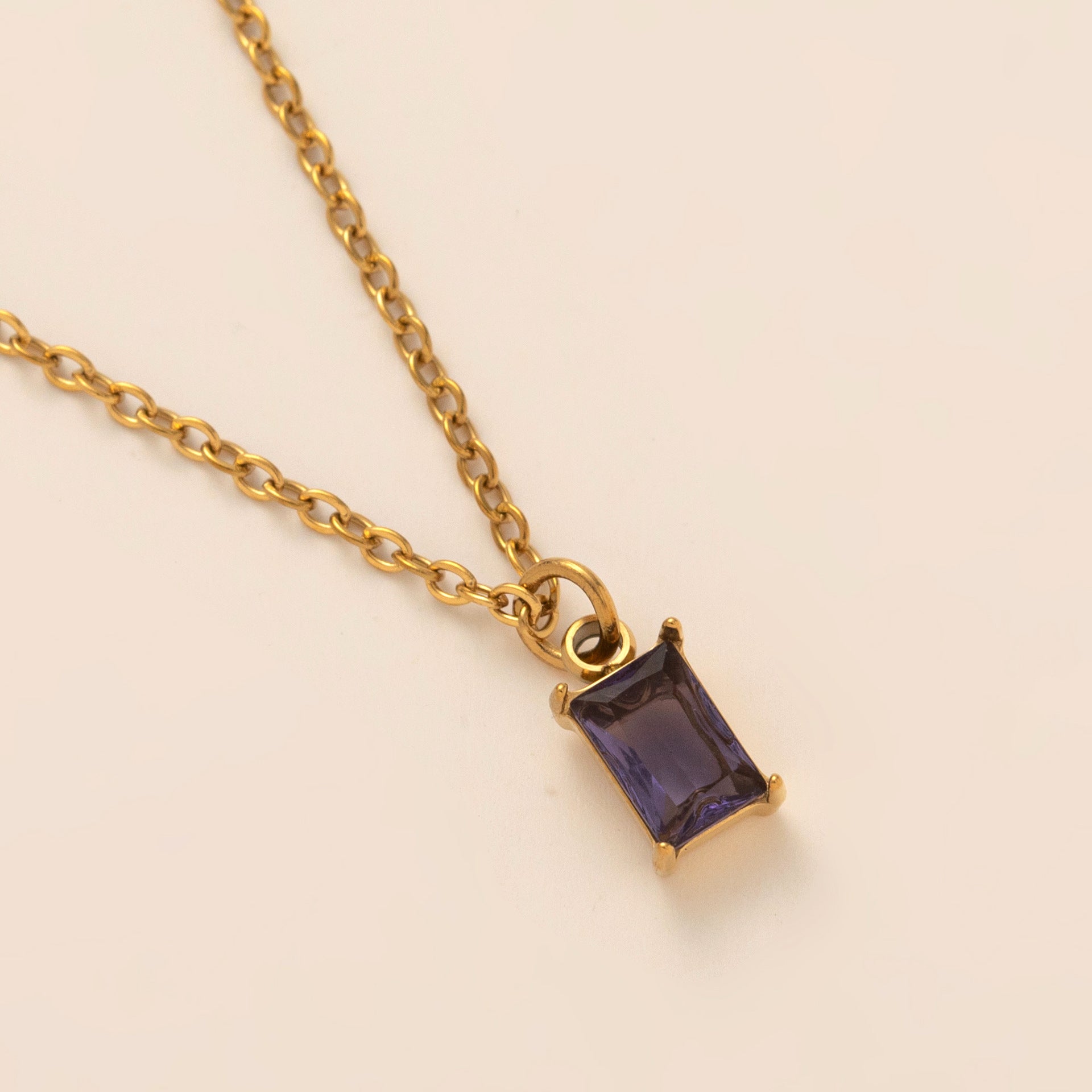 Gold necklace with a purple gemstone pendant on a beige background